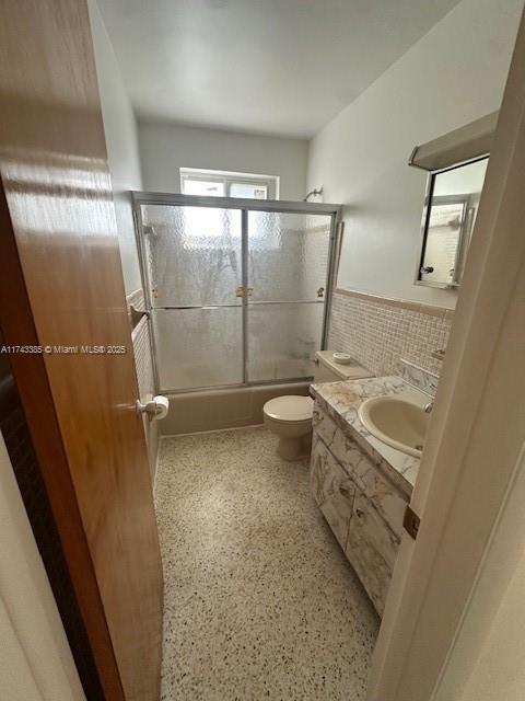 full bathroom with vanity, bath / shower combo with glass door, toilet, and tile walls