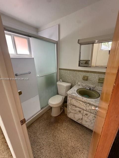 bathroom featuring a shower with door, vanity, tile walls, and toilet