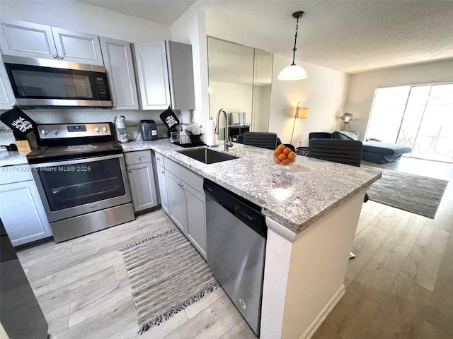 kitchen with sink, hanging light fixtures, stainless steel appliances, light stone countertops, and kitchen peninsula