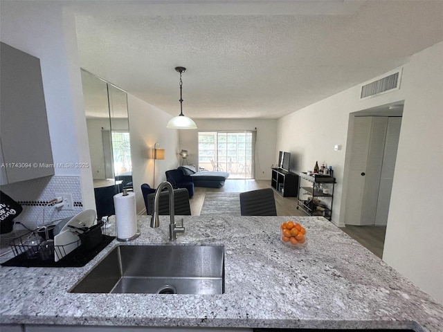 5102 NW 36th St Unit 611, Lauderdale Lakes, FL 33319 - kitchen featuring a sink, light stone countertops, open floor plan, a textured ceiling, and hanging light fixtures