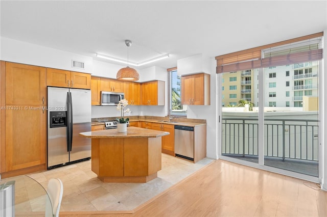 kitchen with hanging light fixtures, stainless steel appliances, sink, and a kitchen island