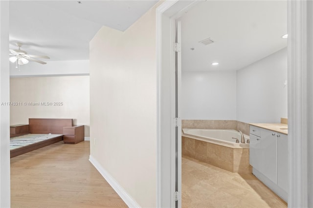 bathroom with vanity, tiled tub, hardwood / wood-style floors, and ceiling fan