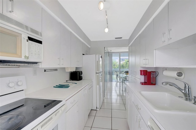 kitchen with sink, white appliances, light tile patterned floors, rail lighting, and white cabinetry