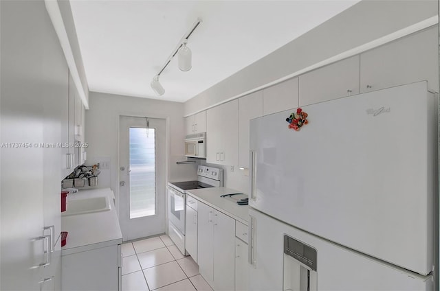 kitchen featuring sink, white appliances, light tile patterned floors, rail lighting, and white cabinetry