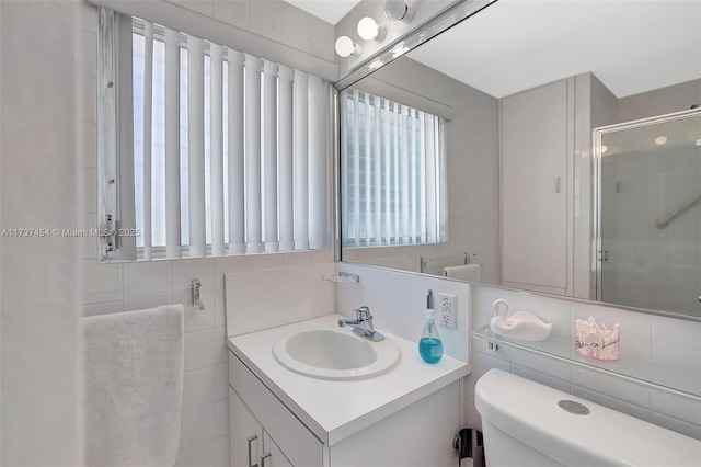 bathroom featuring vanity, toilet, a shower with door, and tile walls