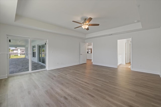 empty room featuring a tray ceiling, ceiling fan, and light wood-type flooring