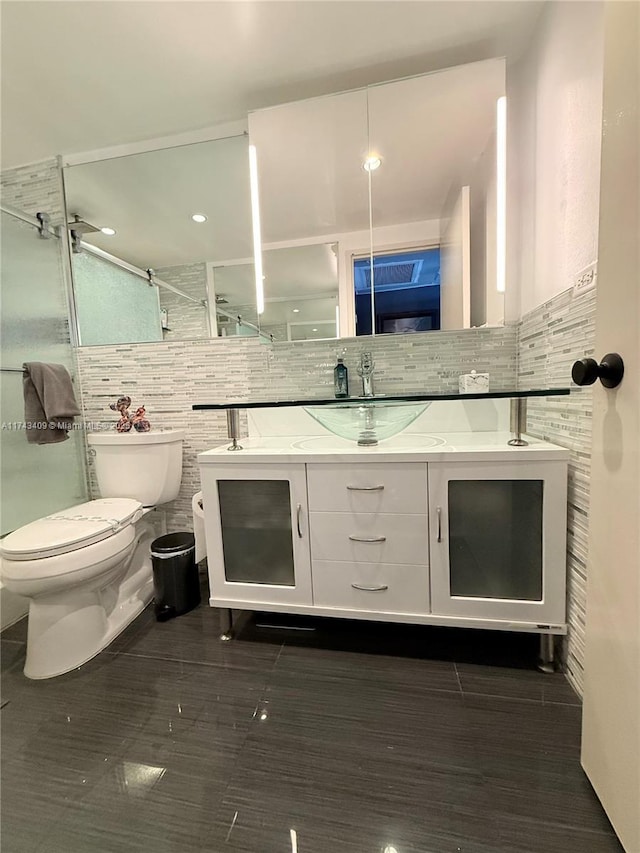 bathroom with a shower with door, vanity, tile walls, and toilet