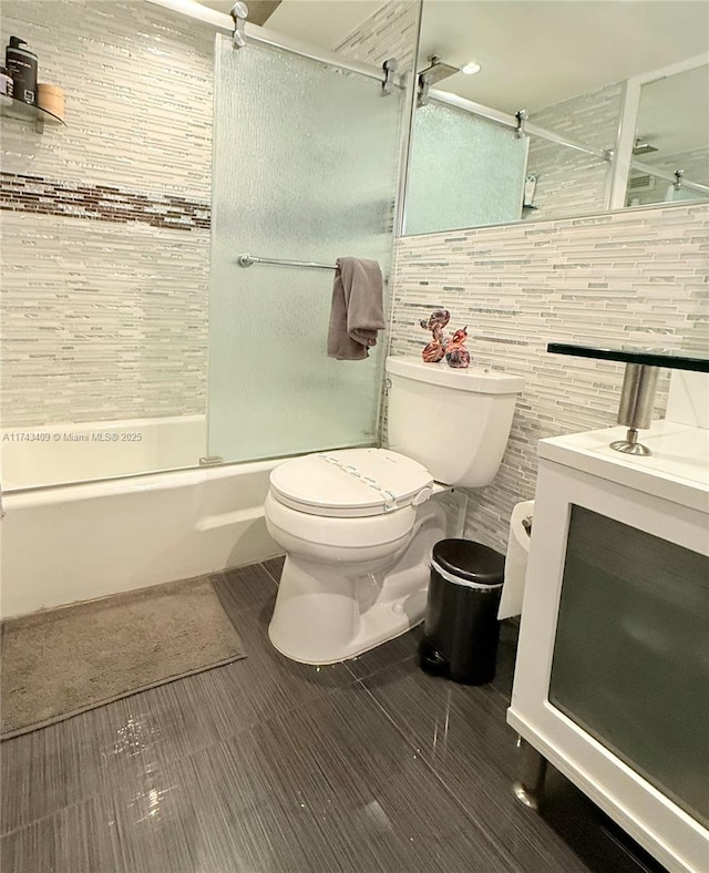 full bathroom with tile walls, enclosed tub / shower combo, vanity, toilet, and tile patterned floors