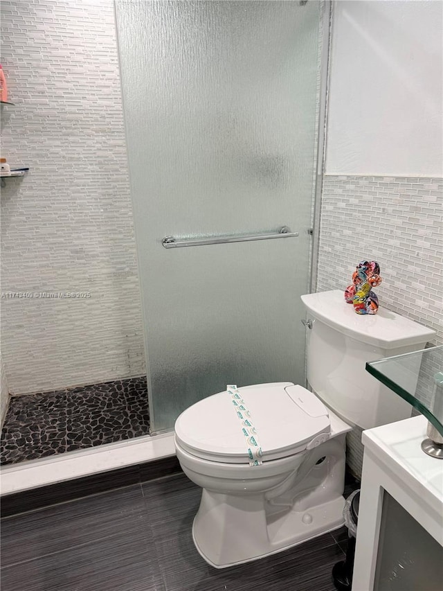 bathroom with tile walls, vanity, toilet, and tiled shower