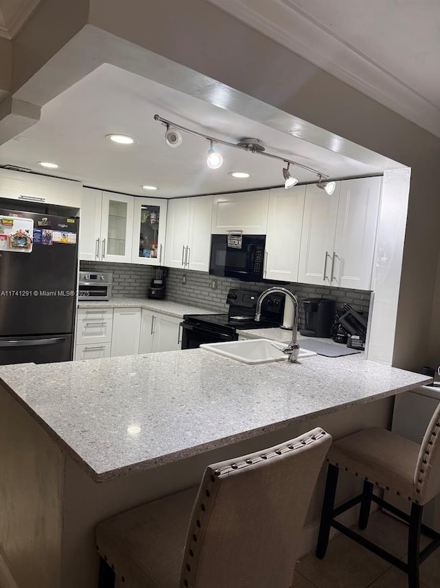 9050 NW 28th St Unit 110, Coral Springs, FL 33065 - kitchen featuring glass insert cabinets, a peninsula, white cabinetry, black appliances, and backsplash