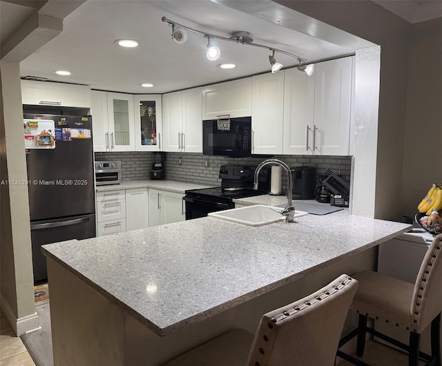 9050 NW 28th St Unit 110, Coral Springs, FL 33065 - kitchen featuring a peninsula, glass insert cabinets, backsplash, white cabinets, and black appliances