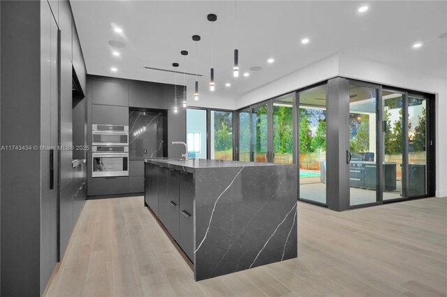 kitchen featuring dark stone countertops, pendant lighting, light wood-type flooring, and a spacious island