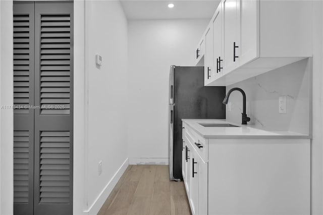 kitchen featuring sink, light hardwood / wood-style flooring, stainless steel refrigerator, and white cabinets