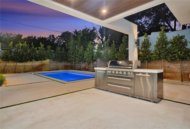 pool at dusk featuring an outdoor kitchen, area for grilling, and a patio area