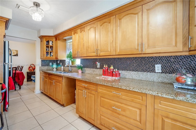 kitchen with light tile patterned flooring, light stone countertops, sink, and backsplash