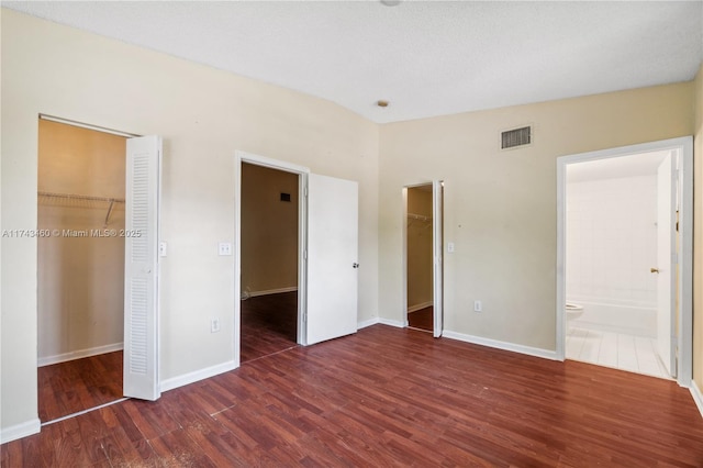 unfurnished bedroom featuring dark wood-type flooring, connected bathroom, a spacious closet, and a closet