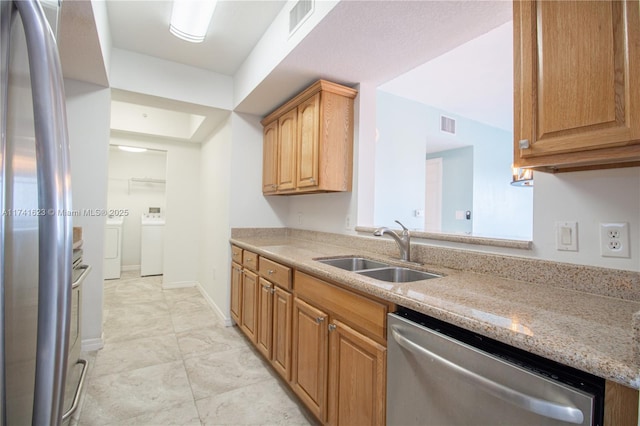 kitchen with sink, light stone countertops, independent washer and dryer, and appliances with stainless steel finishes