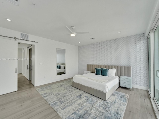 bedroom featuring ceiling fan, a barn door, and light hardwood / wood-style floors