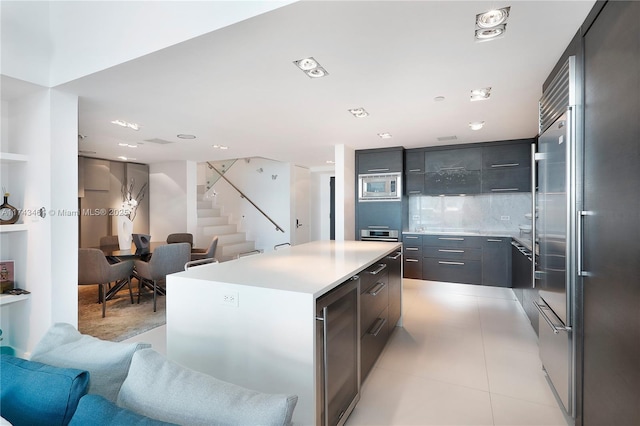 kitchen with light tile patterned flooring, stainless steel microwave, wine cooler, decorative backsplash, and a center island