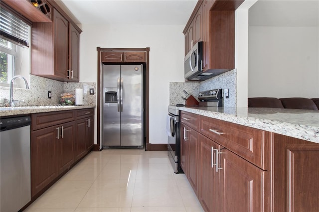 kitchen with light tile patterned flooring, sink, backsplash, light stone counters, and stainless steel appliances