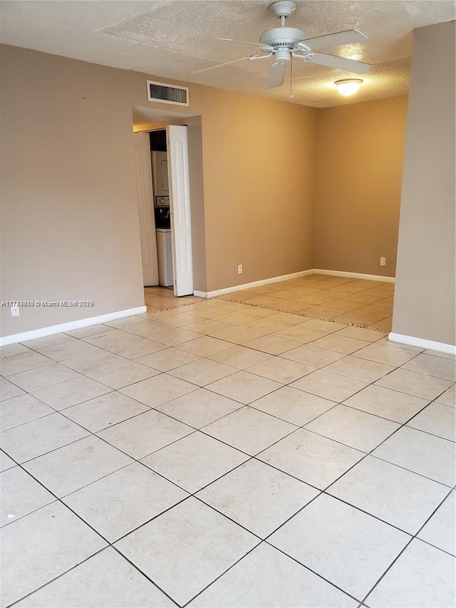 tiled spare room with ceiling fan, stacked washer and clothes dryer, and a textured ceiling