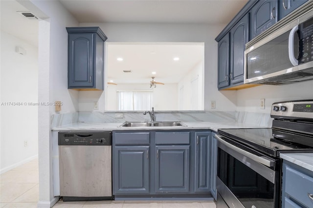 kitchen featuring sink, appliances with stainless steel finishes, light stone countertops, blue cabinets, and light tile patterned flooring