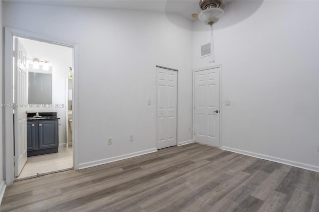 unfurnished bedroom with connected bathroom, hardwood / wood-style floors, sink, ceiling fan, and a closet