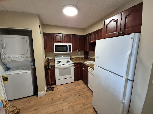 kitchen with sink, light hardwood / wood-style flooring, a textured ceiling, white appliances, and stacked washer / dryer