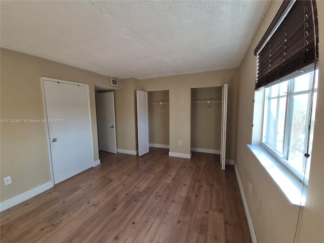 unfurnished bedroom featuring two closets, wood-type flooring, and a textured ceiling