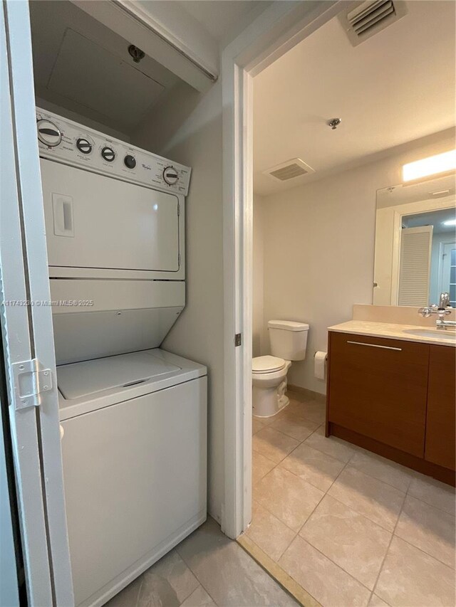 bathroom with tile patterned floors, stacked washer and clothes dryer, toilet, and vanity