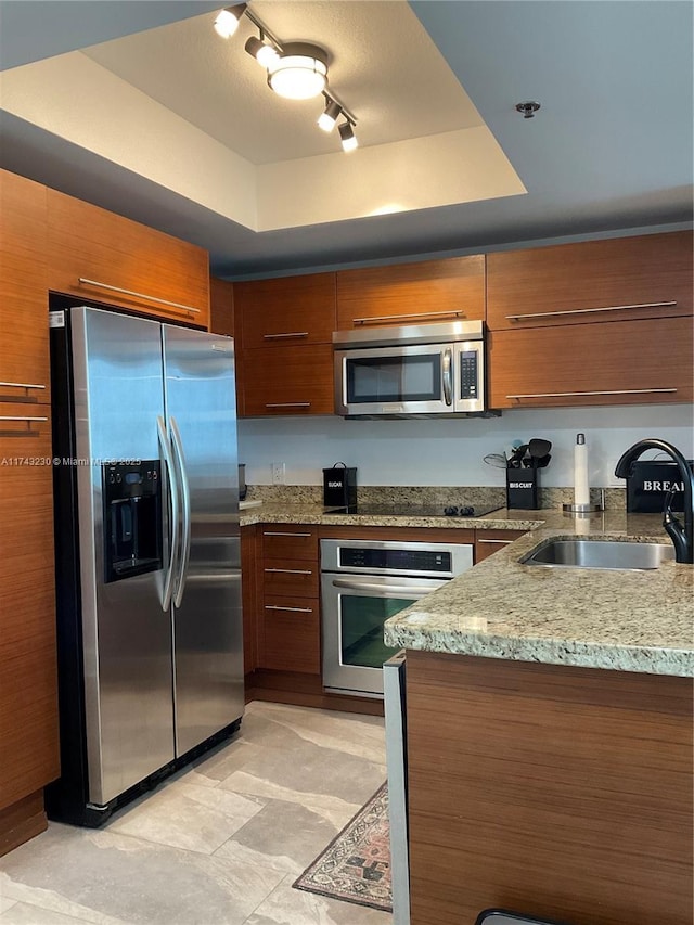 kitchen featuring stainless steel appliances, a raised ceiling, sink, and light stone countertops