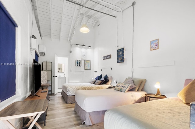 bedroom featuring beam ceiling, light hardwood / wood-style floors, an AC wall unit, and a high ceiling