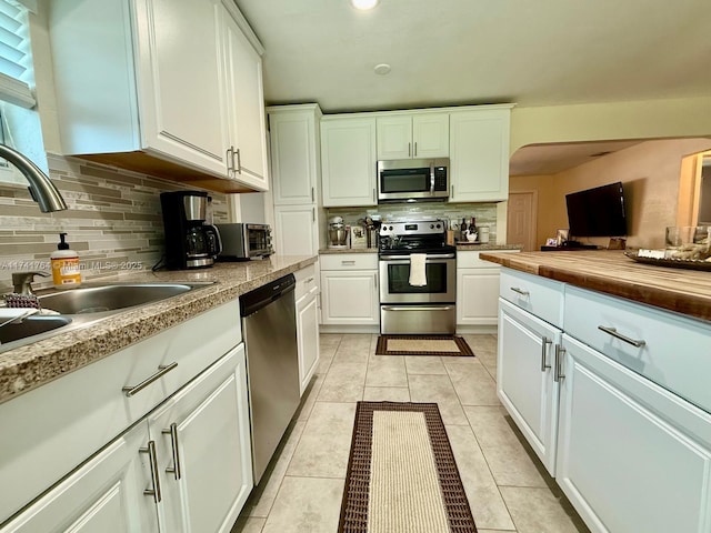 kitchen featuring white cabinetry, stainless steel appliances, tasteful backsplash, and light tile patterned floors