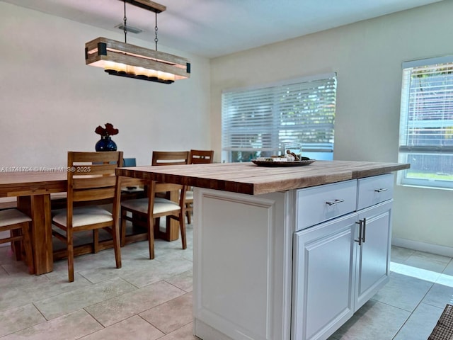 kitchen featuring butcher block countertops, light tile patterned floors, a kitchen island, pendant lighting, and white cabinets