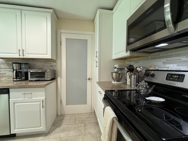 kitchen with light tile patterned flooring, light stone counters, stainless steel appliances, decorative backsplash, and white cabinets