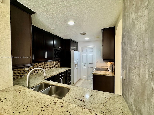 kitchen featuring sink, tasteful backsplash, dark brown cabinetry, light stone countertops, and white fridge with ice dispenser