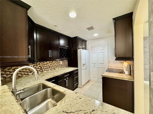 kitchen with sink, light stone counters, tasteful backsplash, dark brown cabinetry, and white fridge with ice dispenser