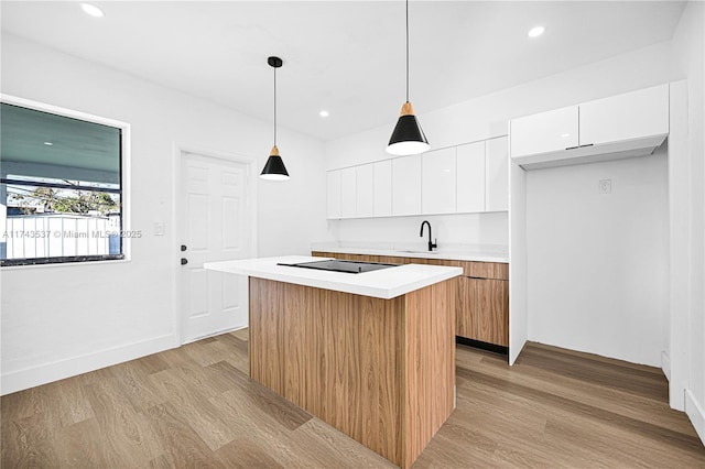 kitchen with light hardwood / wood-style flooring, a kitchen island, pendant lighting, black electric stovetop, and white cabinets