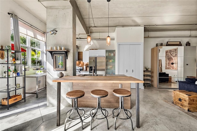 kitchen featuring butcher block counters, hanging light fixtures, stainless steel fridge, and a kitchen bar