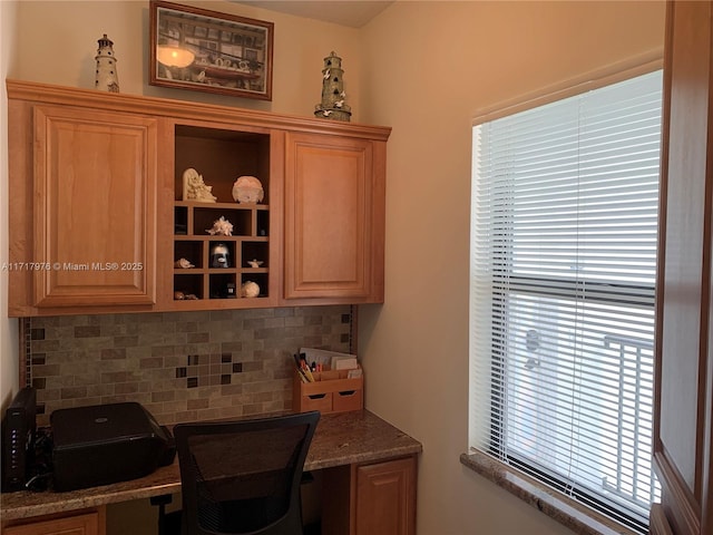 bar featuring backsplash, a wealth of natural light, built in desk, and dark stone counters