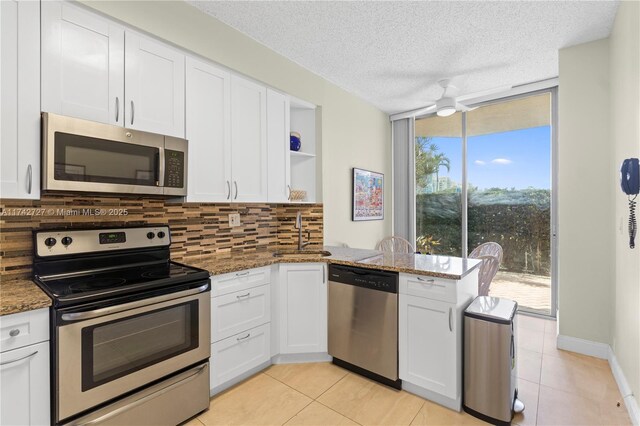 kitchen featuring dark stone countertops, stainless steel appliances, tasteful backsplash, white cabinets, and kitchen peninsula