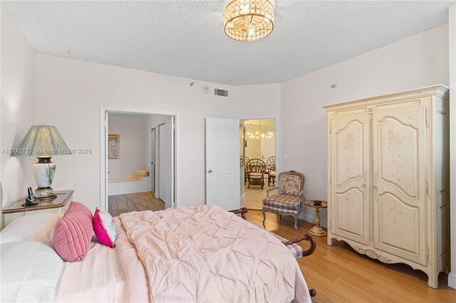 bedroom featuring ensuite bathroom, a chandelier, light hardwood / wood-style floors, and a textured ceiling