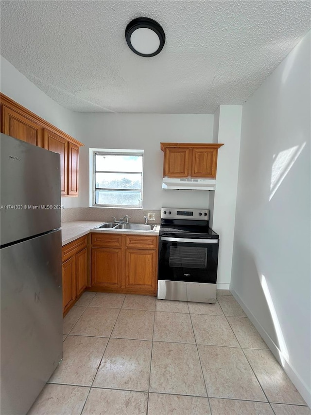 kitchen with stainless steel appliances, sink, light tile patterned floors, and a textured ceiling