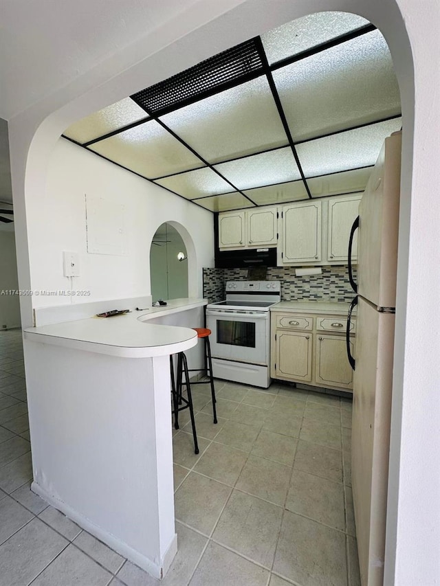 kitchen featuring light tile patterned flooring, white appliances, kitchen peninsula, and tasteful backsplash