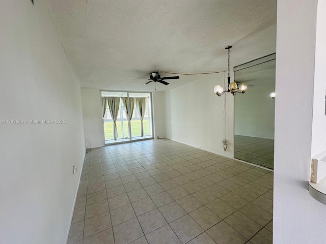 empty room featuring light tile patterned floors, ceiling fan with notable chandelier, and a textured ceiling