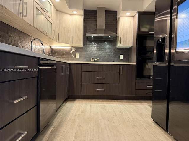 kitchen with light wood-type flooring, light countertops, black appliances, and wall chimney exhaust hood