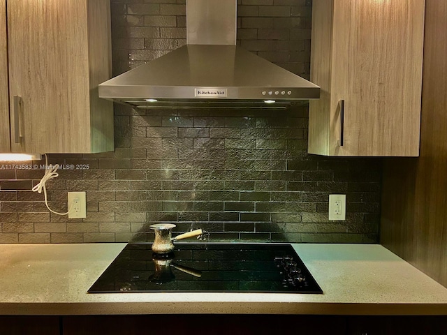 kitchen featuring light countertops, wall chimney range hood, black cooktop, and backsplash