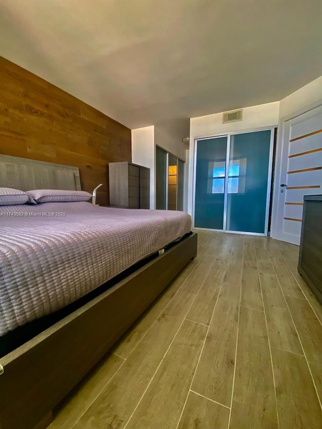 bedroom featuring wood walls, visible vents, and wood finished floors