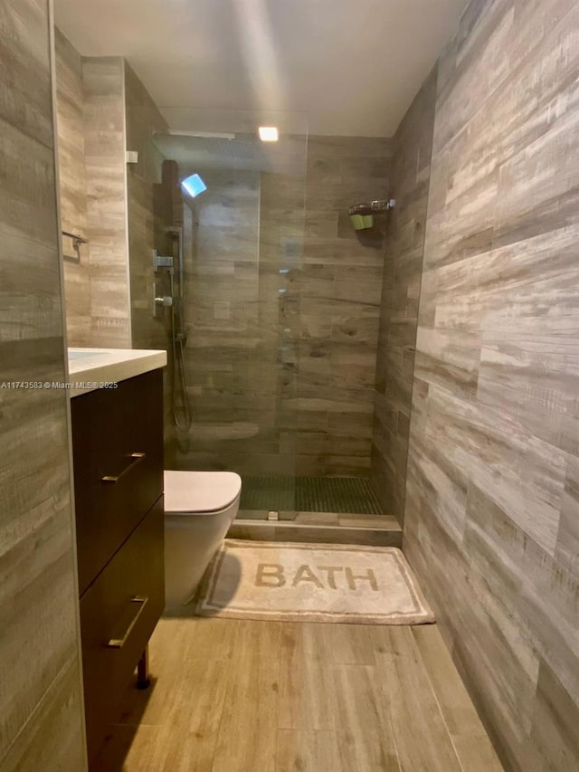 bathroom with a tile shower, vanity, toilet, and wood finished floors