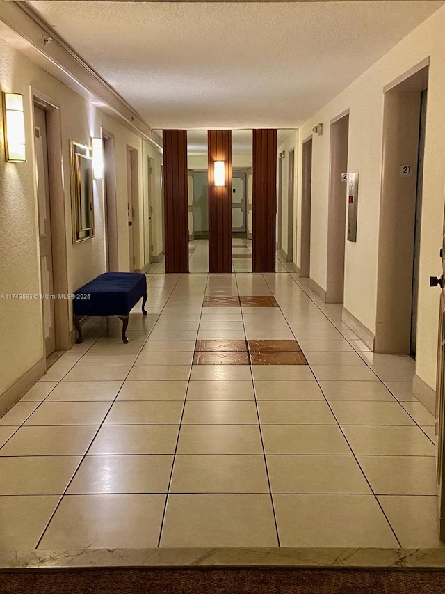 hall featuring a textured ceiling, light tile patterned flooring, and elevator